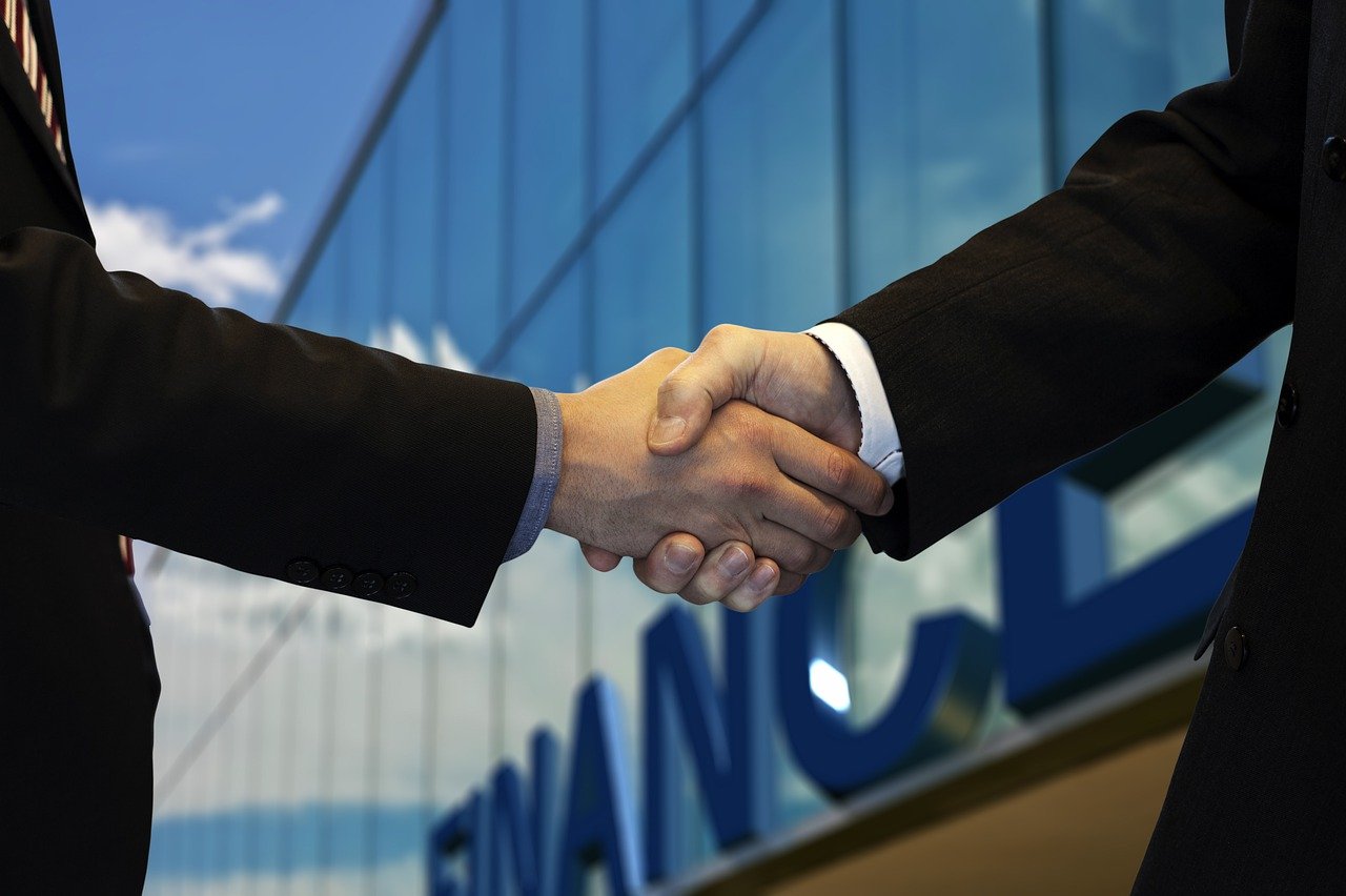 Two people shaking hands in front of a financial office building